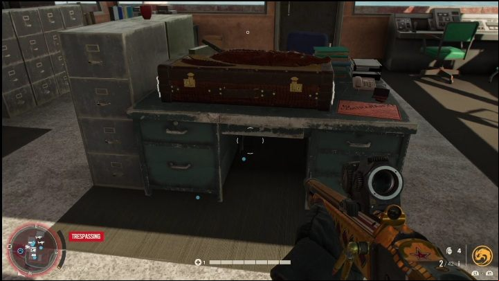 The crate sits on a metal desk in a room near the edge of a body of water - Far Cry 6: Rifles, Unique weapons - list - Unique weapons - Far Cry 6 Guide