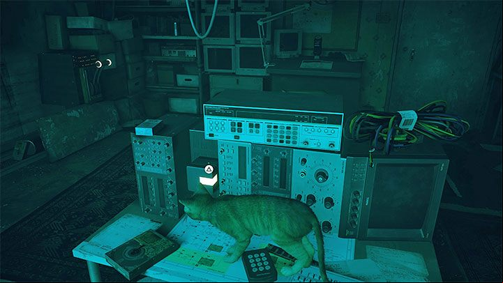 The second object is on the central desk and is used to power one of the computers - Stray: The puzzle with B-12s body - The Flat - Puzzles - Stray Guide, Walkthrough
